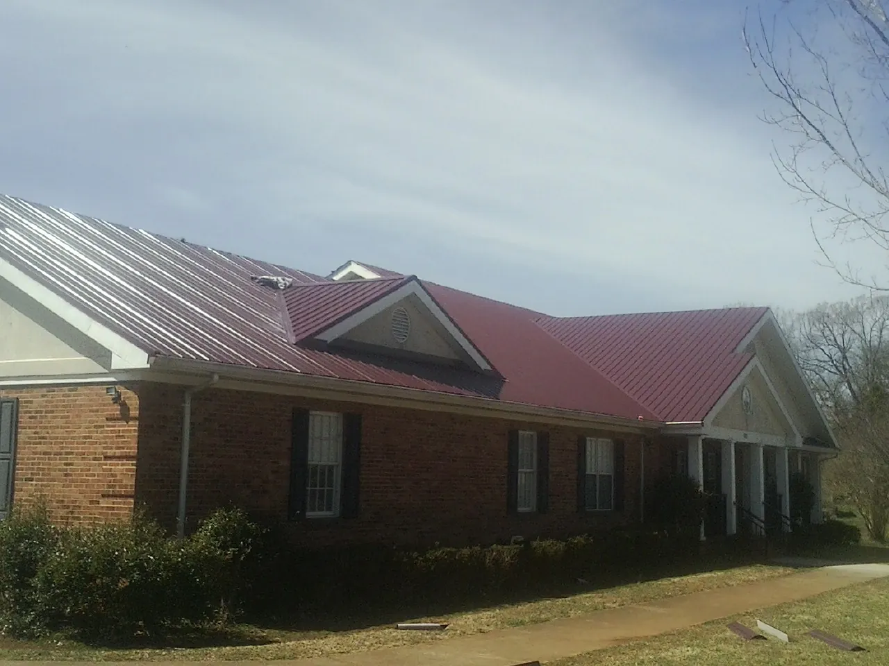 Red metal roof with gabled entries on a long brick building, from a Hail Damage Roof Repair job in Milton Mills