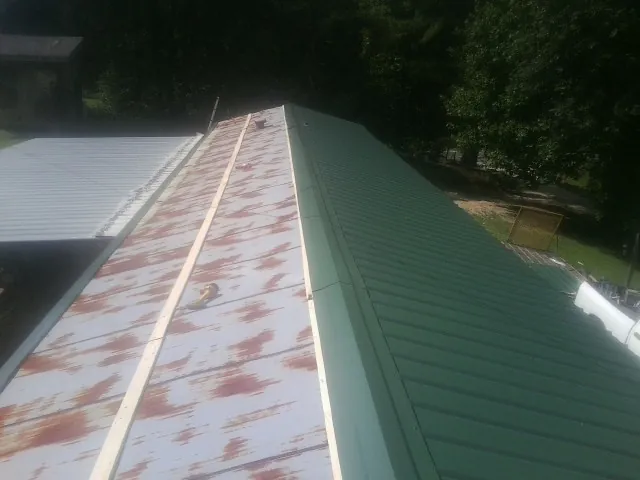 Old rusted panels beside newly installed green metal roofing — Wind Damage Roof Repair by Roofing Brothers in Milton Mills