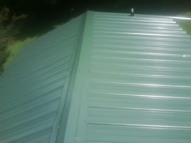 New green metal panels meeting at the ridge of a roof — Flat Roof Repair work by our crew in Milton Mills