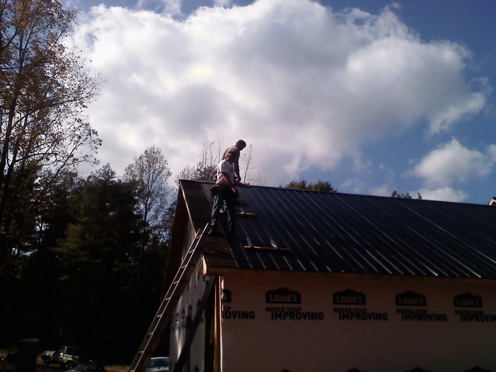 Roofer fastening dark metal panels high against a cloudy sky, from a Roof Inspection job in Milton Mills
