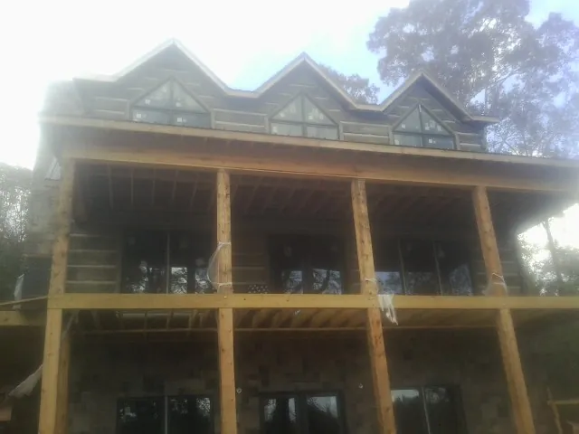Dormers and porch framing on a large log home under construction — Roof Coating work by our crew in Milton Mills