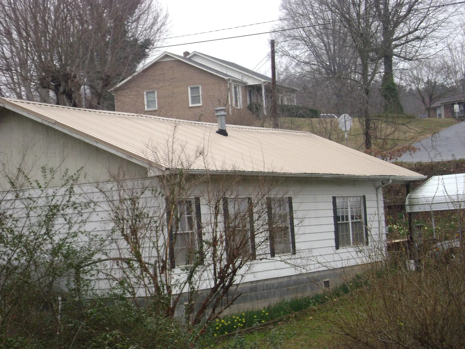 Tan metal roof on a white sided house set into a hillside — Commercial Roofing by Roofing Brothers in Milton Mills