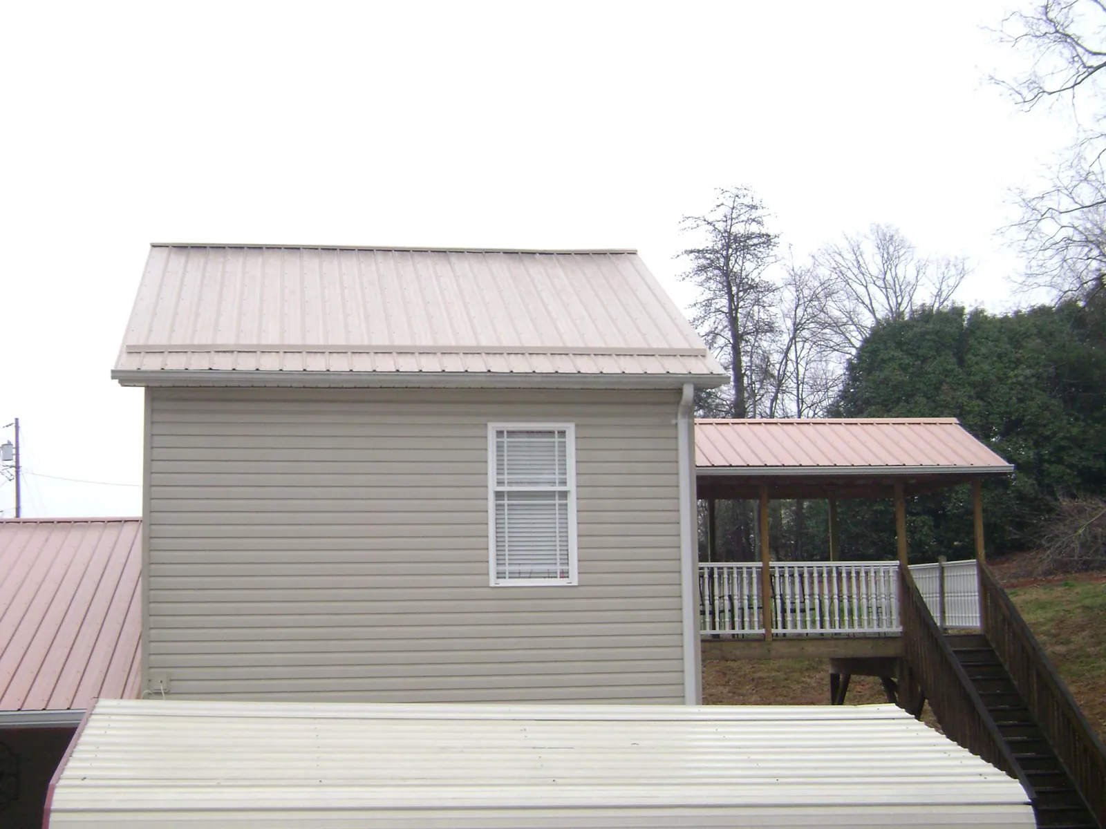 Tan metal roofs on a two story addition and attached porch, from a Roof Replacement job in Milton Mills